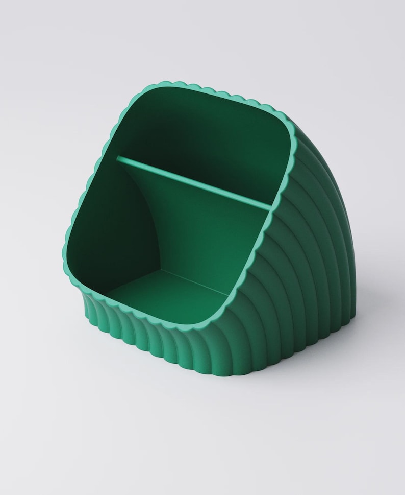 May include: A green desk tidy with a scalloped edge design. The organiser has a curved shape with a divider inside, creating two compartments. The exterior features vertical ridges, adding texture. The colour is a vibrant, solid green.