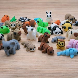 Op de afbeelding: Een verzameling kleurrijke dierfiguren-gummen, waaronder een panda, een olifant, een beer en een konijn, gerangschikt op een lichtbruin houten oppervlak. De gummen zijn in verschillende kleuren en maten.