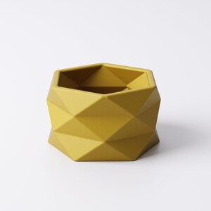 May include: A geometric, mustard-yellow planter with a faceted design. The hexagonal planter has a modern, minimalist aesthetic, suitable for small plants or succulents. The planter is made of a solid material and has a matte finish.