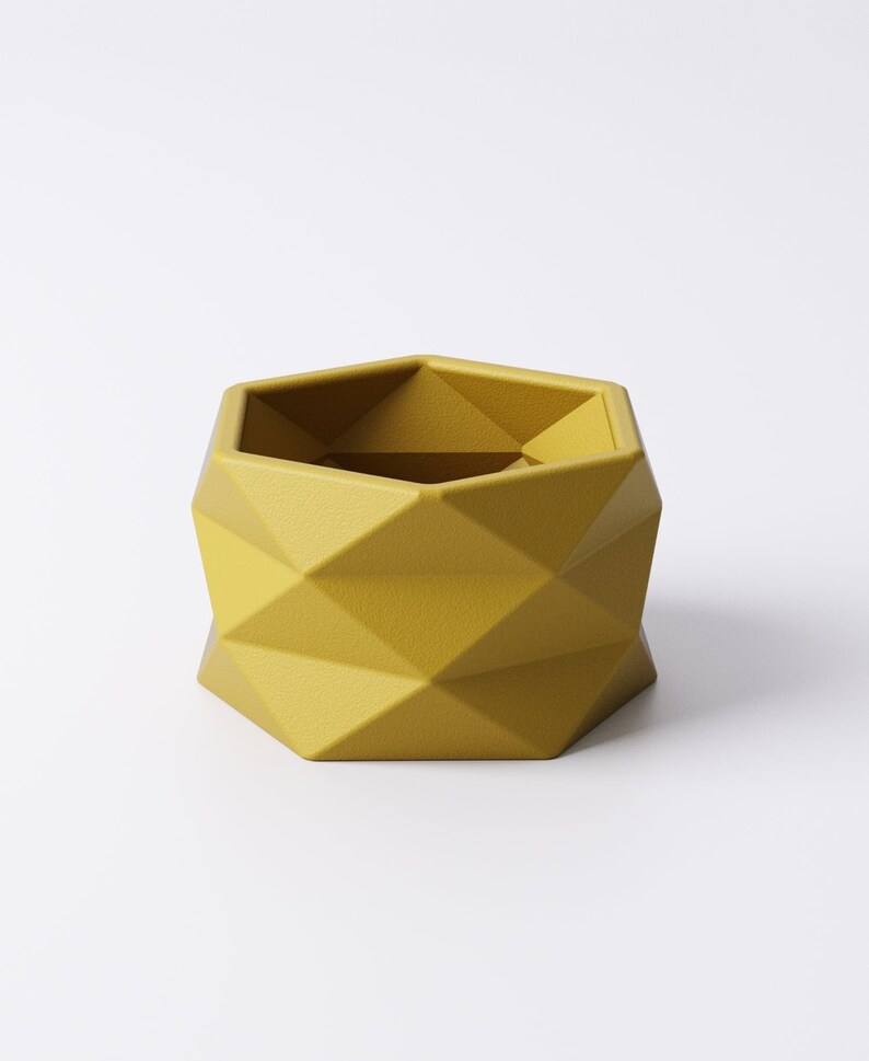 May include: A geometric, mustard-yellow planter with a faceted design. The hexagonal planter has a modern, minimalist aesthetic, suitable for small plants or succulents. The planter is made of a solid material and has a matte finish.