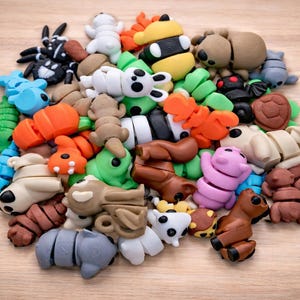 Op de afbeelding: Een verzameling kleurrijke dierfiguren-gummen in verschillende kleuren, waaronder bruin, wit, blauw, oranje, groen en roze. De gummen zijn gerangschikt in een hoop op een lichtbruin houten oppervlak.