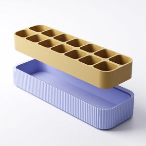 May include: A two-piece ice cube tray set. The top tray is mustard yellow with 12 square compartments. The bottom tray is lavender with vertical ribbed sides. The trays are rectangular and designed to stack.