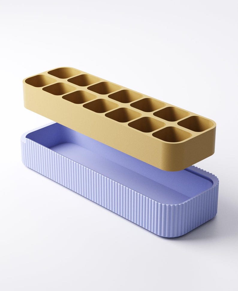 May include: A two-piece ice cube tray set. The top tray is mustard yellow with 12 square compartments. The bottom tray is lavender with vertical ribbed sides. The trays are rectangular and designed to stack.
