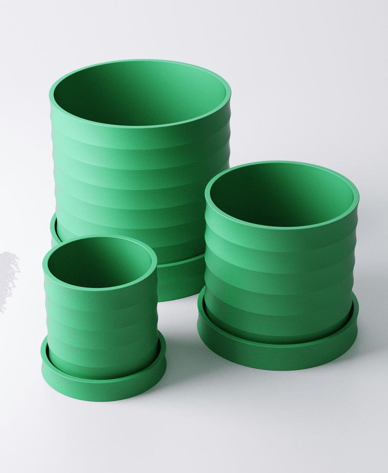 Op de afbeelding: Drie groene cilindrische bloempotten van verschillende maten. Elke pot heeft horizontale geribbelde details en staat op een bijpassende ronde basis. De potten hebben een levendige, effen groene kleur.