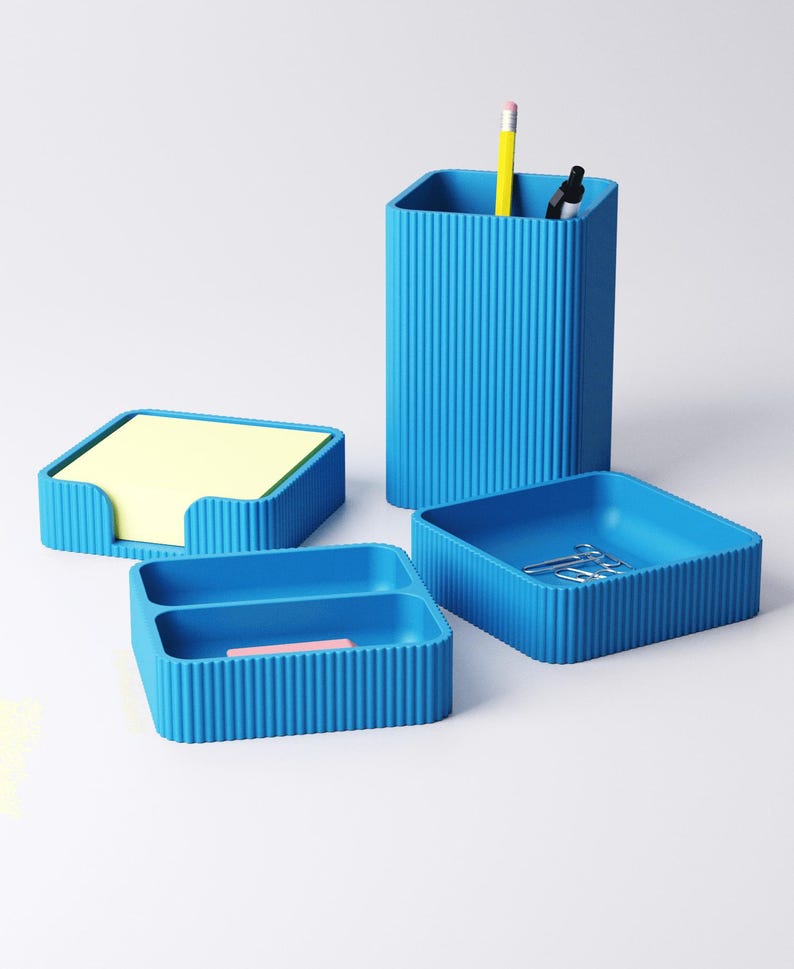 May include: A set of four matching blue desk organizers. The set includes a pencil holder with a yellow pencil and black marker, a square tray with paperclips, a small tray with a pink eraser, and a notepad holder with yellow sticky notes.