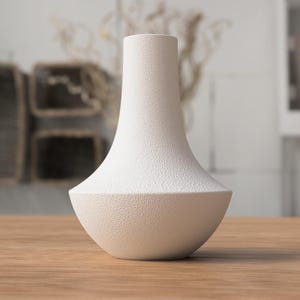 May include: A white, textured vase with a unique shape. The vase has a wide, rounded base that tapers to a narrow neck. The surface has a speckled texture. The vase is sitting on a wooden table.
