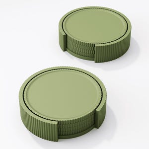 May include: Two olive green coasters with a ridged, cylindrical design. Each coaster has a flat, circular top and a textured, corrugated edge. The coasters are stacked, showcasing their layered construction. The background is plain white.