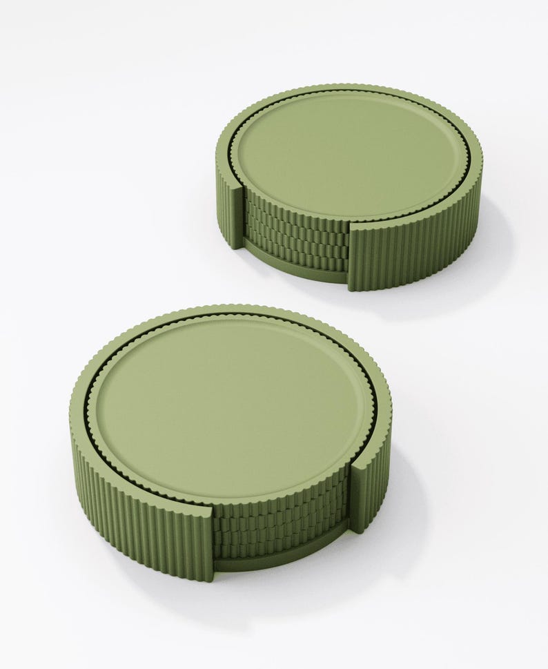 May include: Two olive green coasters with a ridged, cylindrical design. Each coaster has a flat, circular top and a textured, corrugated edge. The coasters are stacked, showcasing their layered construction. The background is plain white.