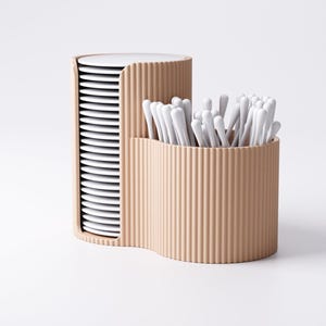 May include: A beige, corrugated container with two compartments. One holds a stack of white plates, the other holds a collection of white cotton swabs. The design is modern and minimalist, suitable for bathroom or kitchen organization.