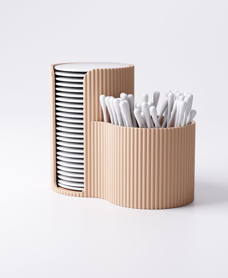 May include: A beige, corrugated container with two compartments. One holds a stack of white plates, the other holds a collection of white cotton swabs. The design is modern and minimalist, suitable for bathroom or kitchen organization.