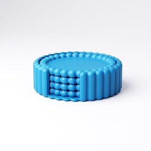 May include: A bright blue, round coaster set. The coasters have a textured, ridged edge and a central design of stacked, spherical shapes. The set is made of a solid, opaque material and is presented against a white background.
