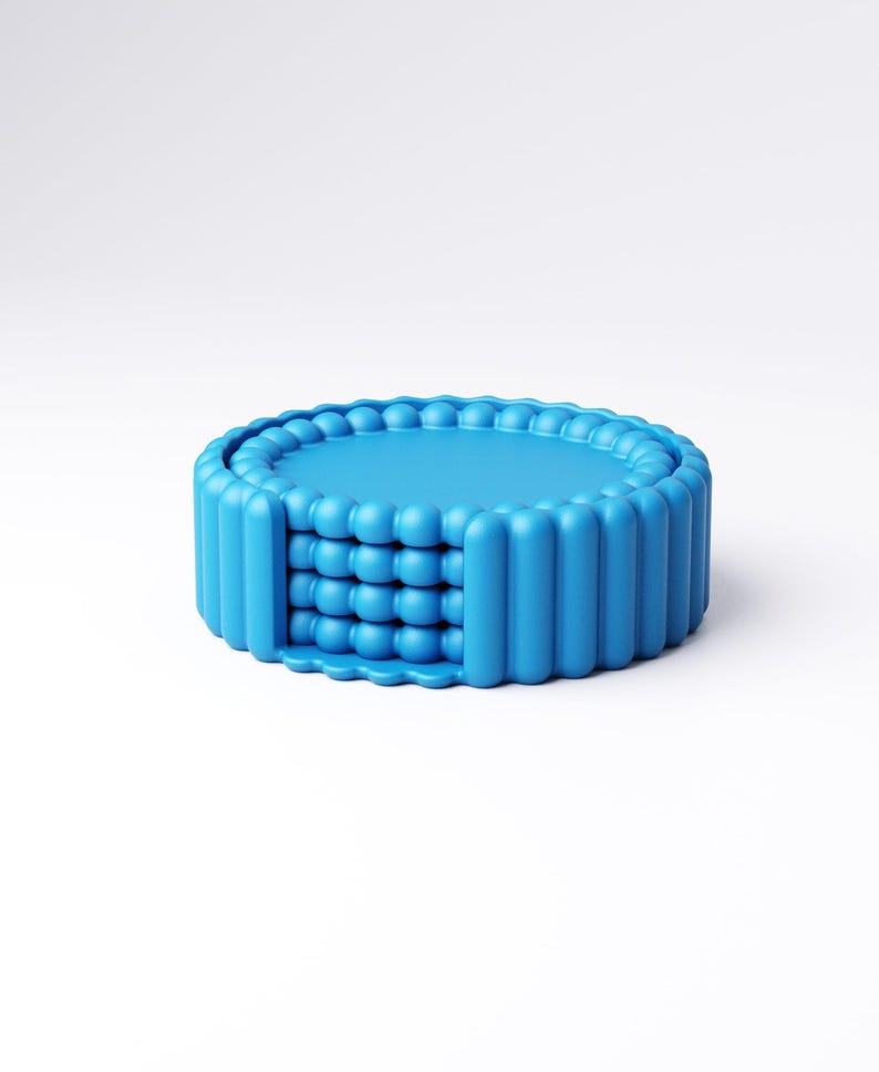 May include: A bright blue, round coaster set. The coasters have a textured, ridged edge and a central design of stacked, spherical shapes. The set is made of a solid, opaque material and is presented against a white background.