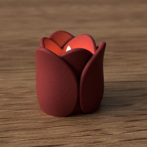 May include: A burgundy-colored tulip-shaped candle holder with a textured surface. The interior glows with a warm orange light, and a small white candle is visible inside. The candle holder is placed on a wooden surface.