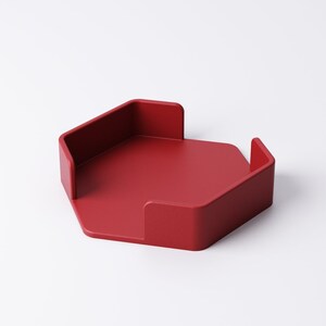 May include: A solid red, hexagonal desk tray with raised sides. The tray has a minimalist design and is likely made of a durable material. The tray is designed to hold small items and keep a desk organized.