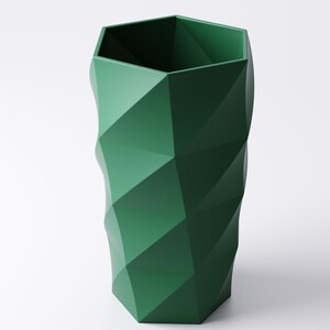 Op de afbeelding: Een hoge, groene geometrische vaas met een facetontwerp. De vaas heeft een zeshoekige opening en een gestructureerde, hoekige buitenkant. De donkergroene kleur en het moderne ontwerp maken het een opvallend decoratief stuk.