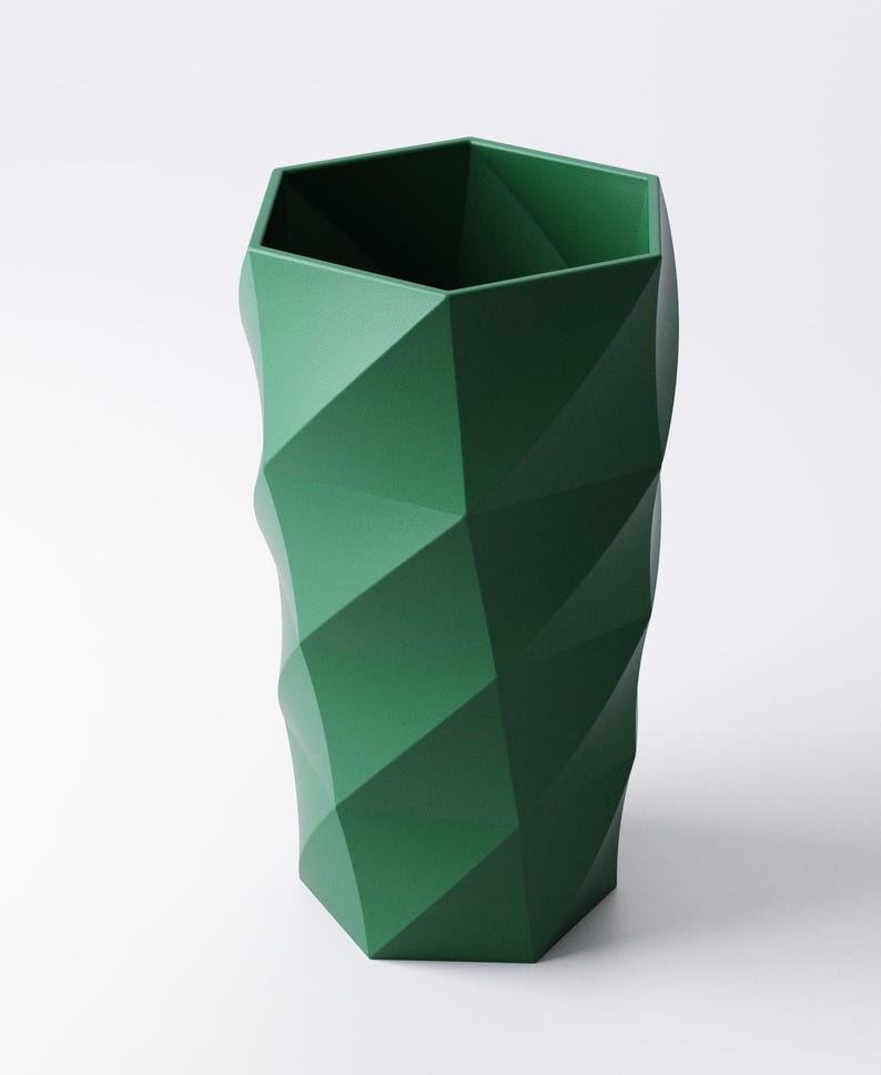 Op de afbeelding: Een hoge, groene geometrische vaas met een facetontwerp. De vaas heeft een zeshoekige opening en een gestructureerde, hoekige buitenkant. De donkergroene kleur en het moderne ontwerp maken het een opvallend decoratief stuk.