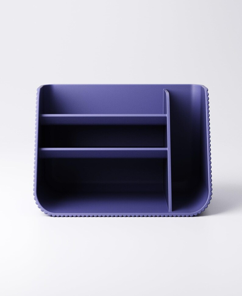 May include: A purple desk organizer with multiple compartments and shelves. The organizer has a rectangular shape with rounded corners and a textured edge. It is designed to hold various office supplies.