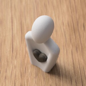Puede incluir: Una escultura abstracta blanca con una cabeza texturizada en forma de huevo y un elemento en forma de coraz&oacute;n gris oscuro en el pecho. La escultura est&aacute; sobre una superficie de madera.