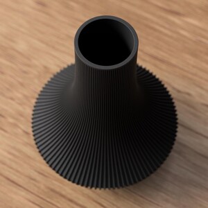 May include: A black vase with a unique, ribbed design. The vase has a wide, flared base that tapers to a narrow neck. The ribbed texture creates a spiral effect, adding visual interest. The vase is made of a solid, matte black material.
