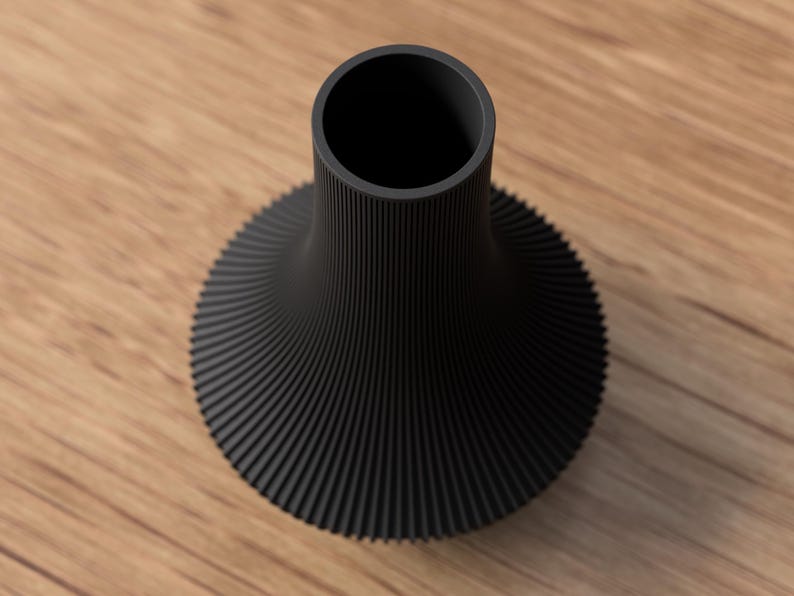May include: A black vase with a unique, ribbed design. The vase has a wide, flared base that tapers to a narrow neck. The ribbed texture creates a spiral effect, adding visual interest. The vase is made of a solid, matte black material.