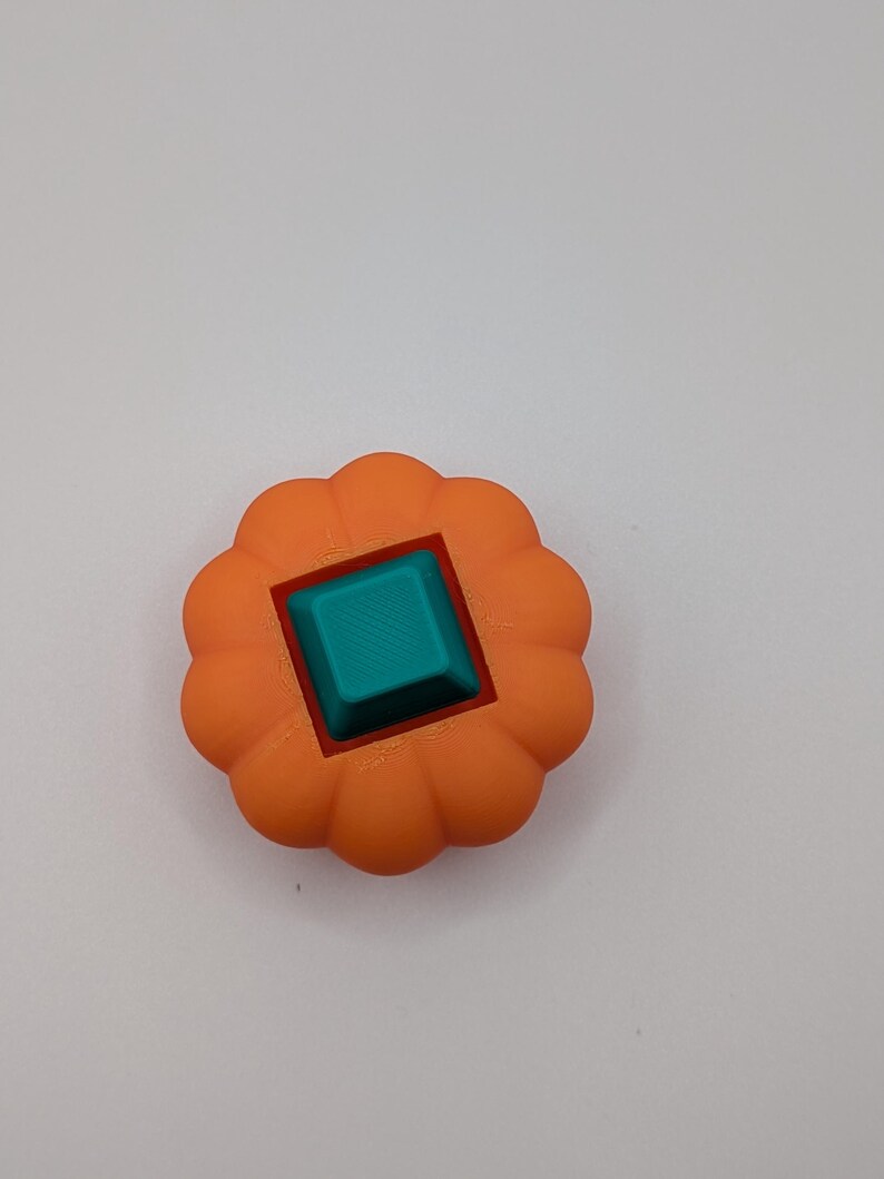 May include: An orange, flower-shaped object with a teal square in the center. The object has a red square border around the teal square. The object is likely a decorative item or a component of a larger design.