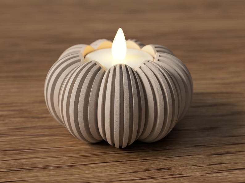 May include: A gray, pumpkin-shaped candle holder with vertical grooves. The candle holder has a white candle with a flickering flame. The candle holder is on a wooden surface.