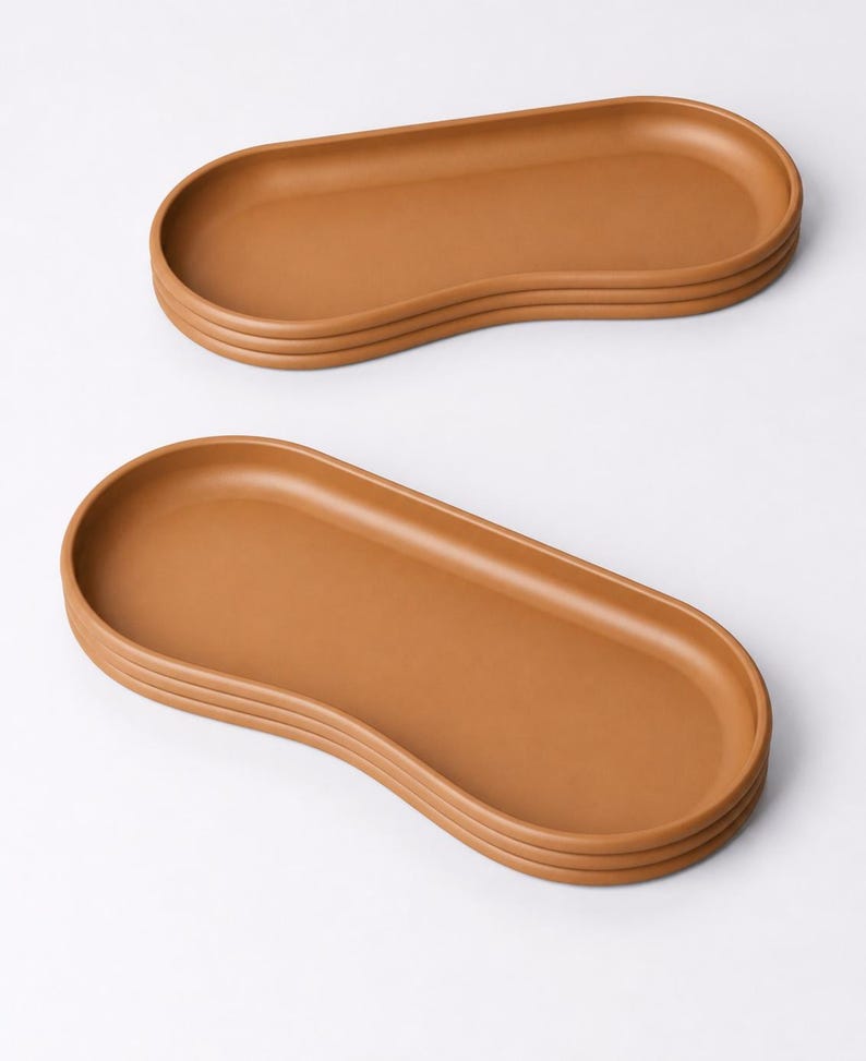 May include: Two brown, oval-shaped serving trays stacked on a white background. The trays have a smooth surface and a raised edge. The trays are a warm, earthy tone, perfect for serving food or displaying items.
