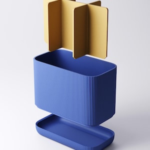 May include: A blue rectangular container with a ribbed exterior texture, featuring a matching blue base tray and a separate gold-colored cross-shaped divider insert that fits inside the main compartment to create four distinct storage sections.