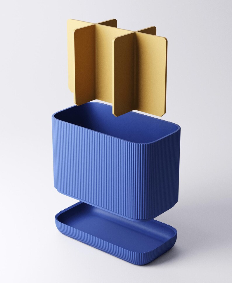May include: A blue rectangular container with a ribbed exterior texture, featuring a matching blue base tray and a separate gold-colored cross-shaped divider insert that fits inside the main compartment to create four distinct storage sections.