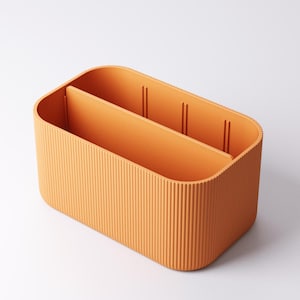 May include: Orange rectangular storage organiser with a ribbed exterior and two internal dividers. The organiser is made of a solid orange material and has a rounded shape. The dividers create three separate compartments.