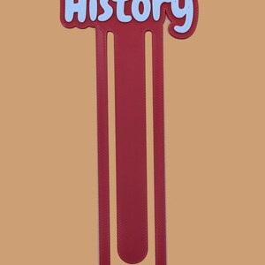 May include: A maroon bookmark featuring a U-shaped design with a textured surface. The top section displays the word History in light blue, rounded, bubble-style lettering with a dark maroon outline, set against a solid, plain background.