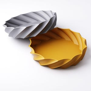 May include: Two decorative bowls with a unique spiral design. One bowl is a light gray color, and the other is a vibrant yellow. The bowls have a wavy, scalloped edge and are set against a white background. These bowls are ideal for home decor.