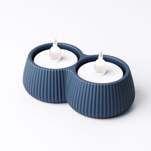 May include: A blue, double-vessel candle holder with a ribbed exterior. Each vessel holds a white disc with a small, white, flame-shaped light. The candle holder is a modern home decor item.