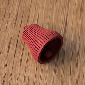 May include: A red bell-shaped object with a small ball inside, resting on a wooden surface. The bell has a series of vertical, curved lines. The bell is made of a solid material and has a small loop at the top.