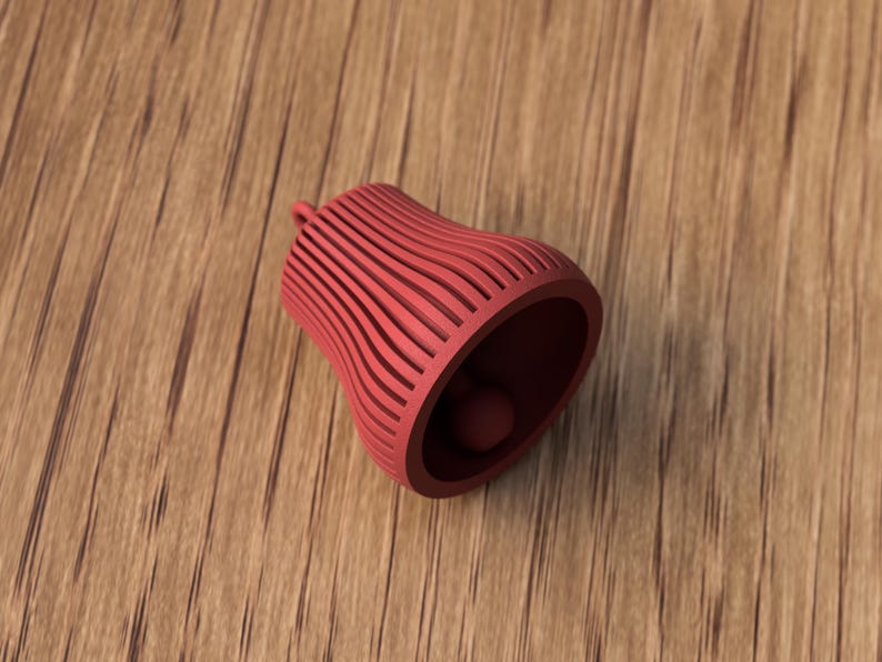 May include: A red bell-shaped object with a small ball inside, resting on a wooden surface. The bell has a series of vertical, curved lines. The bell is made of a solid material and has a small loop at the top.