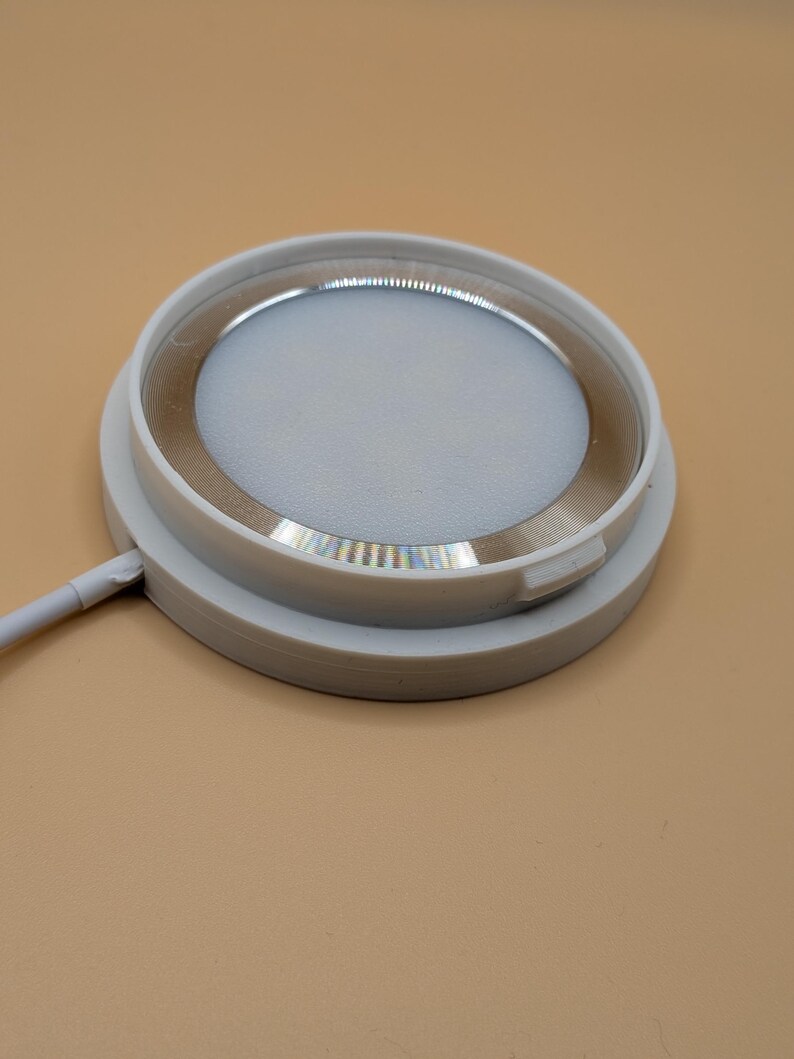 K&ouml;nnte beinhalten: Eine runde, wei&szlig;e LED-Leuchte mit einem silberfarbenen Innenring. Die Leuchte hat ein flaches, kreisf&ouml;rmiges Design und ein wei&szlig;es Netzkabel, das sich von der Seite erstreckt. Die Leuchte ist f&uuml;r Einbauanwendungen konzipiert.