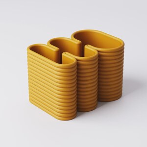 Puede incluir: Objeto decorativo moderno de color amarillo mostaza con un dise&ntilde;o ondulado &uacute;nico. La pieza est&aacute; compuesta por tres secciones verticales conectadas, con una textura acanalada. Las partes superiores redondeadas y la forma general sugieren un jarr&oacute;n o un elemento escult&oacute;rico.