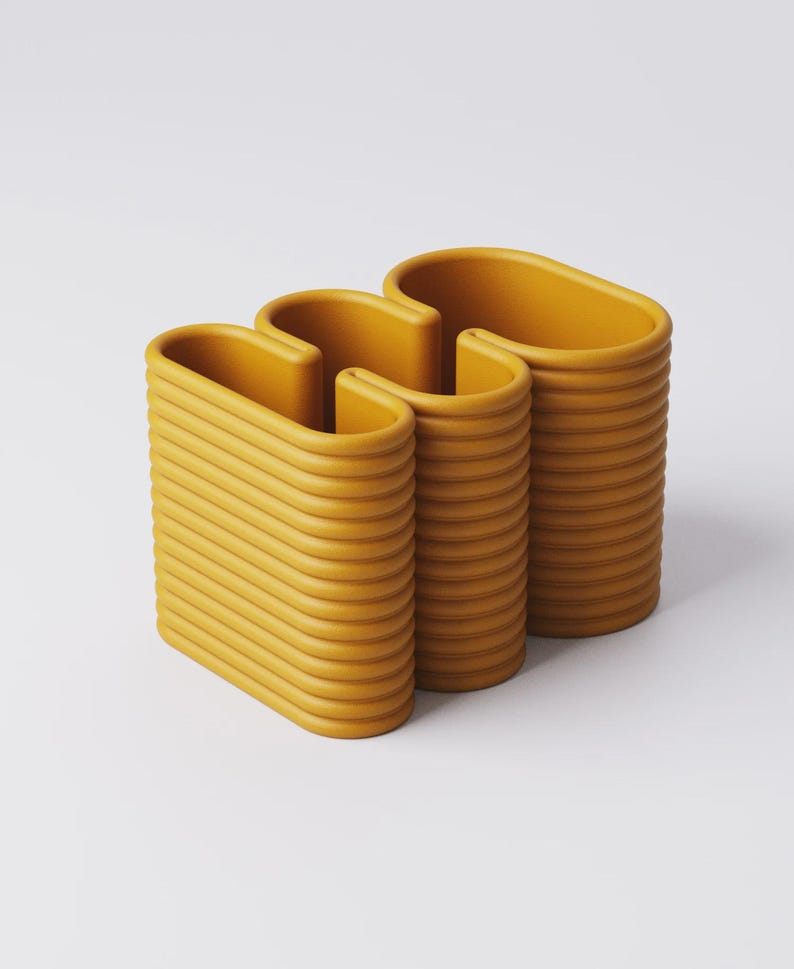 Puede incluir: Objeto decorativo moderno de color amarillo mostaza con un dise&ntilde;o ondulado &uacute;nico. La pieza est&aacute; compuesta por tres secciones verticales conectadas, con una textura acanalada. Las partes superiores redondeadas y la forma general sugieren un jarr&oacute;n o un elemento escult&oacute;rico.