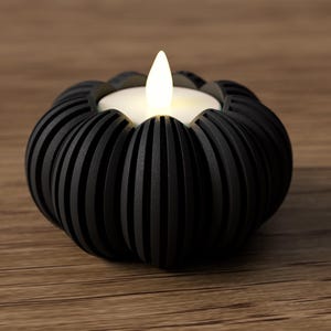 May include: A black, decorative candle holder with a ribbed design, holding a white LED candle with a flickering flame. The candle holder is on a wooden surface, creating a warm, inviting ambiance. The candle holder is approximately 4 inches in diameter.