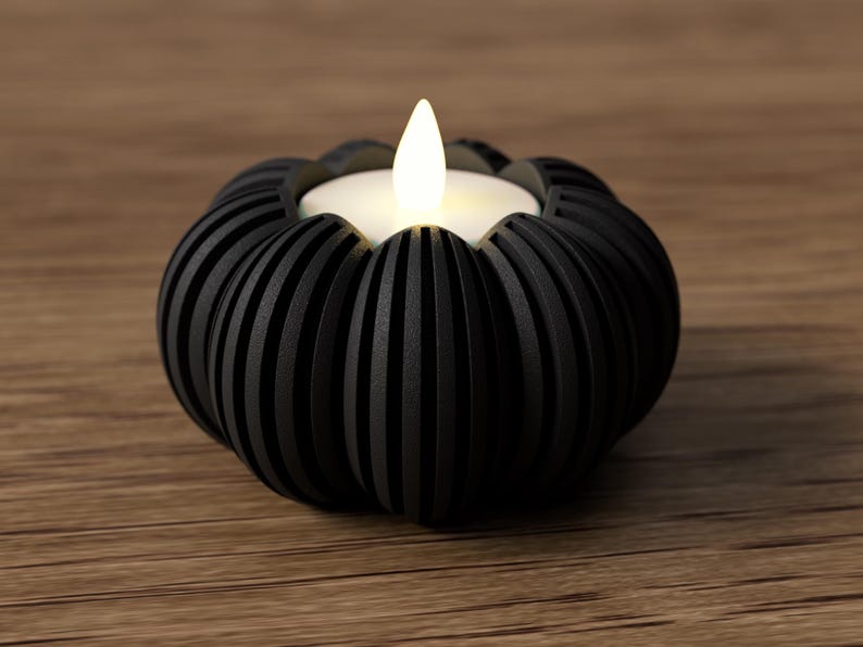 May include: A black, decorative candle holder with a ribbed design, holding a white LED candle with a flickering flame. The candle holder is on a wooden surface, creating a warm, inviting ambiance. The candle holder is approximately 4 inches in diameter.