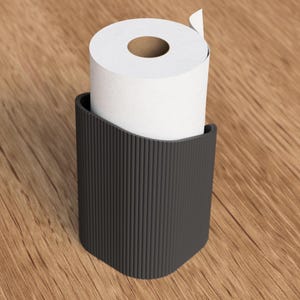 Op de afbeelding: Een zwarte, geribbelde toiletpapierhouder met een rol wit toiletpapier. De houder heeft een gebogen bovenkant en een rechthoekige vorm. De houder is gemaakt van donker materiaal en staat op een houten oppervlak.