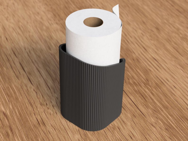Op de afbeelding: Een zwarte, geribbelde toiletpapierhouder met een rol wit toiletpapier. De houder heeft een gebogen bovenkant en een rechthoekige vorm. De houder is gemaakt van donker materiaal en staat op een houten oppervlak.