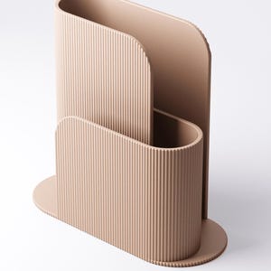 May include: A beige desk organiser with a modern, ribbed design. The organiser has a curved shape with a base and a tall, open section for storing items. The overall design is minimalist and stylish, suitable for a home office.
