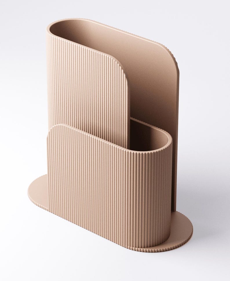 May include: A beige desk organiser with a modern, ribbed design. The organiser has a curved shape with a base and a tall, open section for storing items. The overall design is minimalist and stylish, suitable for a home office.