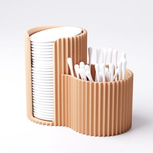 May include: A two-part, light brown, ribbed organizer. One section holds a stack of white, round pads. The other section contains a collection of white, cotton swab applicators. The design is modern and minimalist, suitable for a bathroom or vanity.