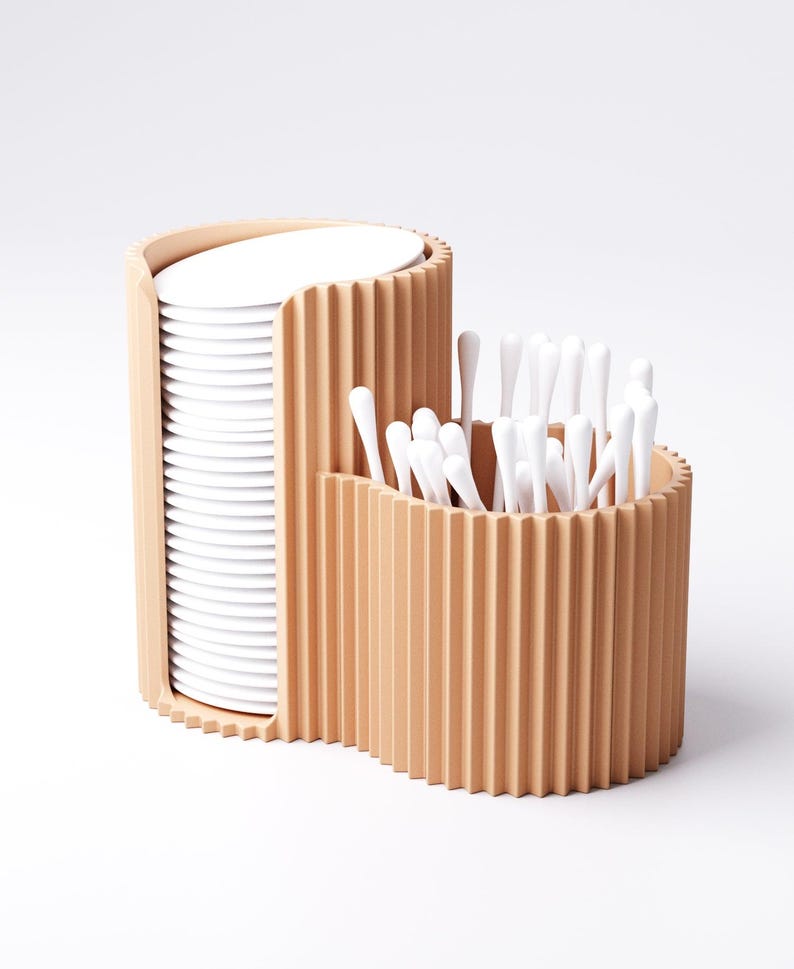 May include: A two-part, light brown, ribbed organizer. One section holds a stack of white, round pads. The other section contains a collection of white, cotton swab applicators. The design is modern and minimalist, suitable for a bathroom or vanity.