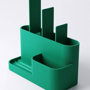 Pode incluir: Um organizador de secret&aacute;ria verde-azulado com uma textura canelada. O organizador tem v&aacute;rios compartimentos, incluindo ranhuras para canetas ou l&aacute;pis e uma bandeja pequena. O design inclui tr&ecirc;s divisores verticais e uma forma arredondada.