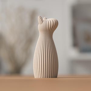 Puede incluir: Un jarr&oacute;n decorativo de madera con un dise&ntilde;o &uacute;nico. El jarr&oacute;n est&aacute; hecho de listones de madera verticales, creando un patr&oacute;n de rayas. La parte superior del jarr&oacute;n tiene una forma curva y est&aacute; sobre una superficie marr&oacute;n.