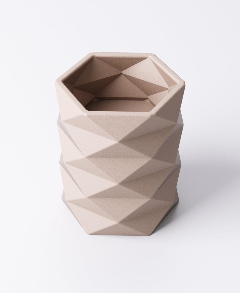 May include: A beige geometric planter with a faceted design. The planter has a hexagonal top and a cylindrical body with a repeating diamond pattern. The neutral color and modern design make it suitable for various decor styles.