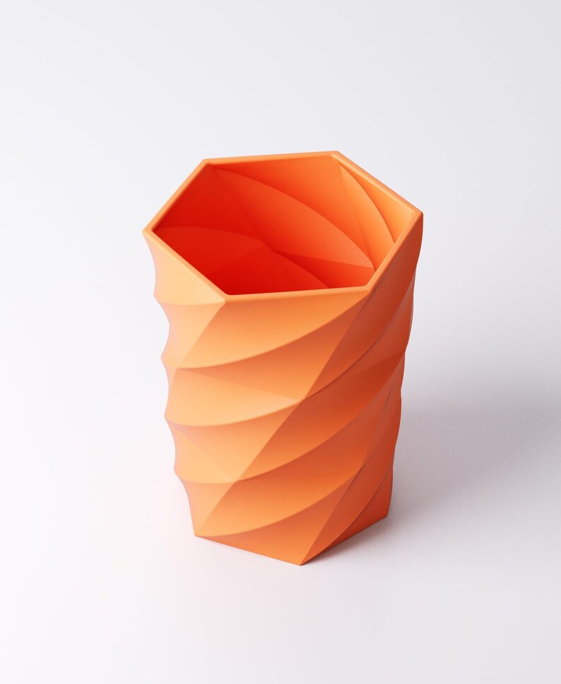 May include: An orange geometric vase with a hexagonal top and a spiraling, textured design. The vase is made of a solid material and has a modern, minimalist aesthetic. The vase is approximately 8 inches tall.